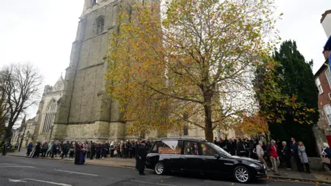 PA Media A black vehicle with a light wooden coffin in the back.