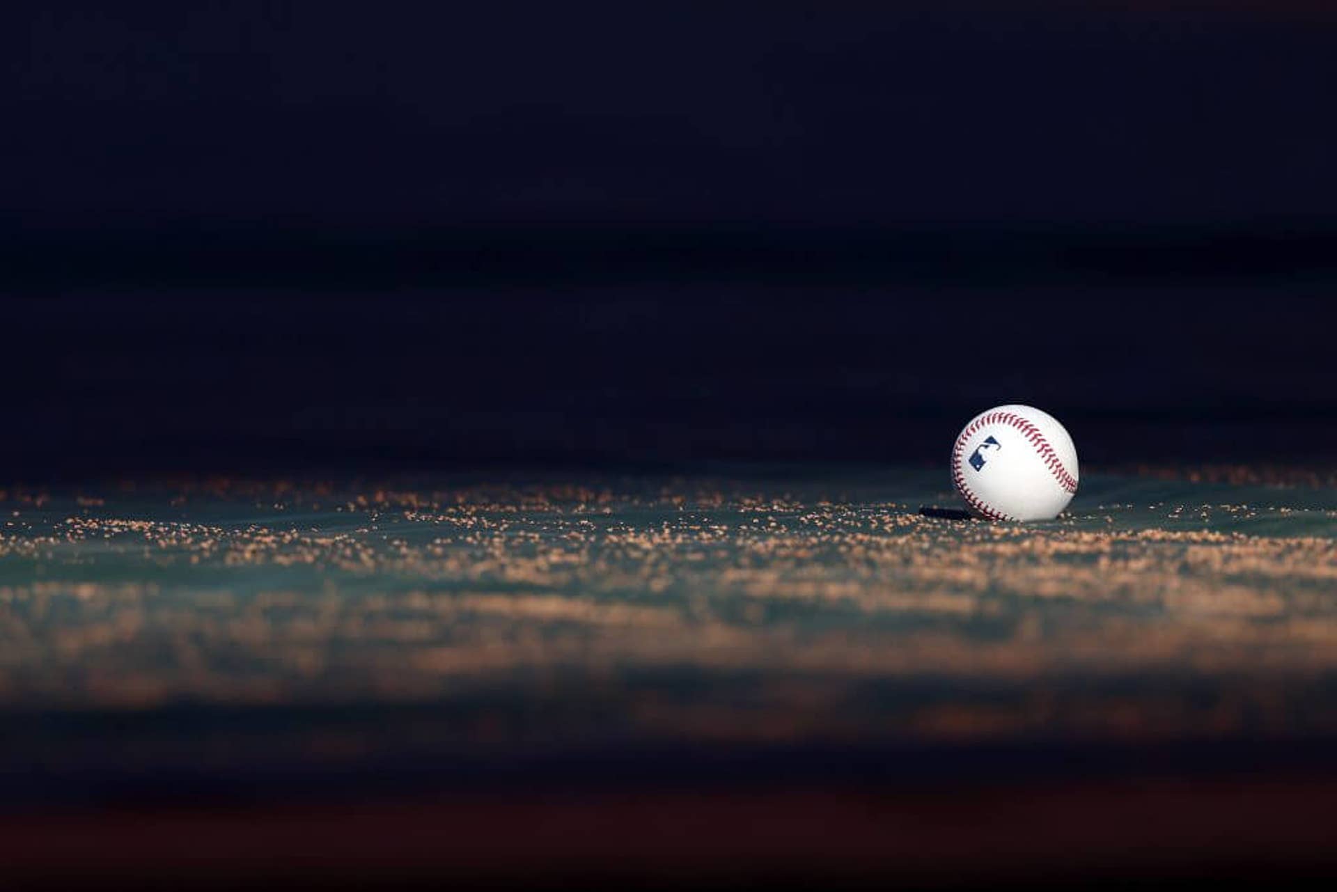 A baseball with the MLB logo rests on the field during a batting practice.