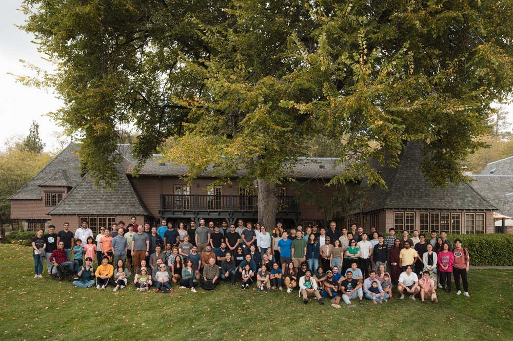 Several people standing in front of a lodge with trees around.