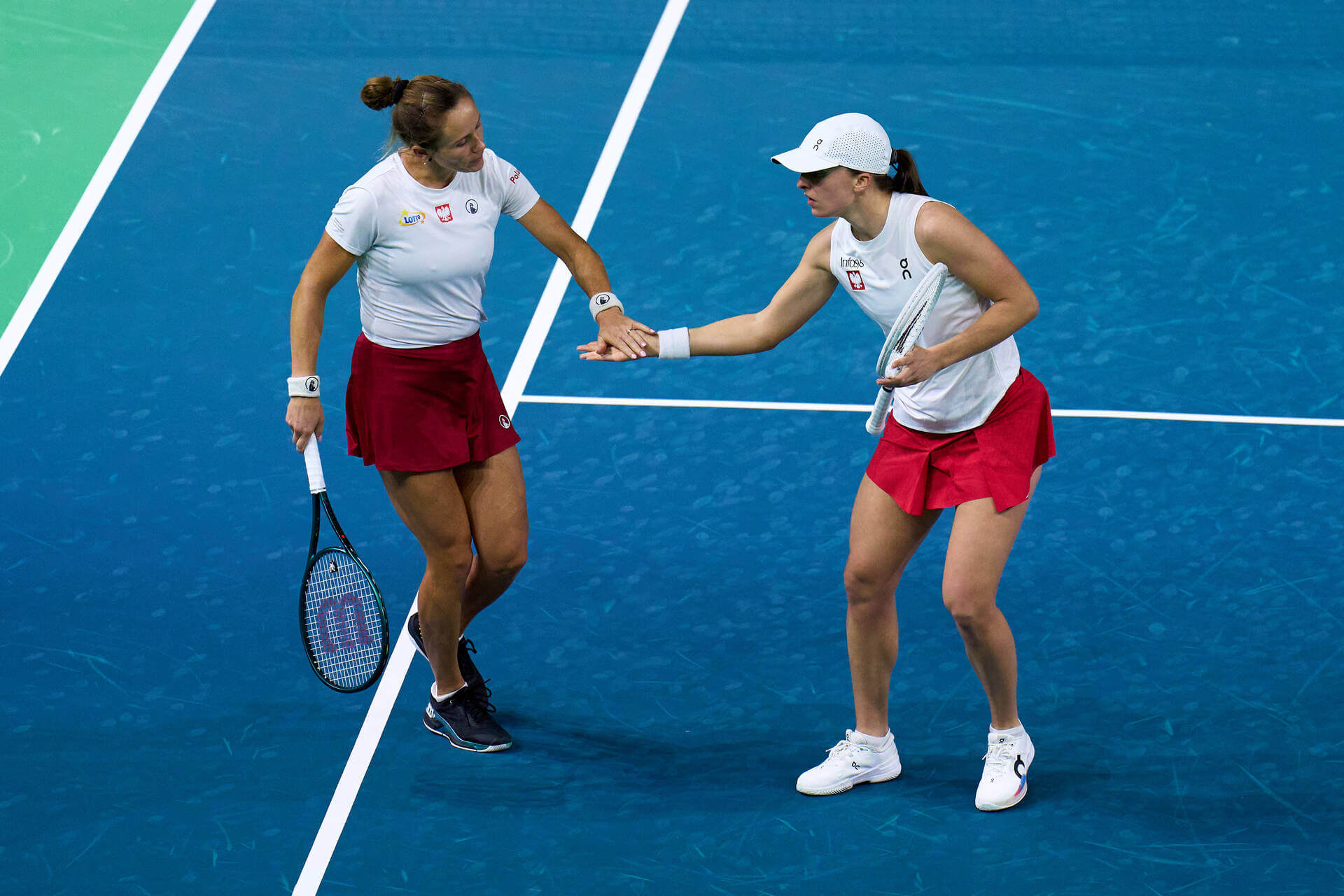 Katarzyna Kawa (left) and Iga Świątek (right) hi-five on a blue tennis court during a doubles match.