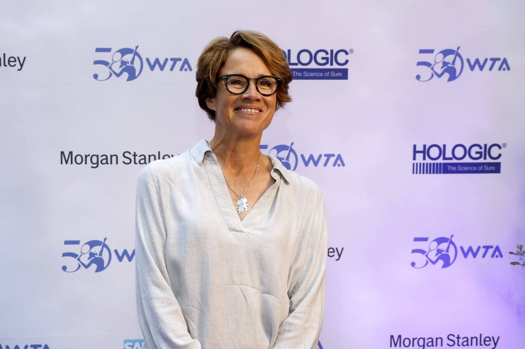 A three-quarter portrait of Mary Carillo against a backdrop of “WTA 50” and sponsor logos.