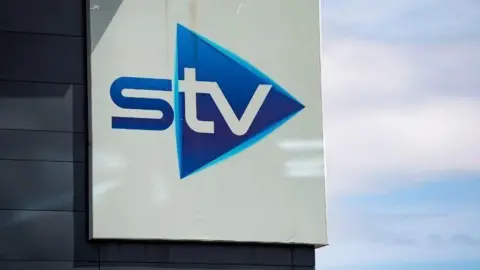 SNS Close up of a blue and white STV sign on a building, photographed against a cloudy blue sky
