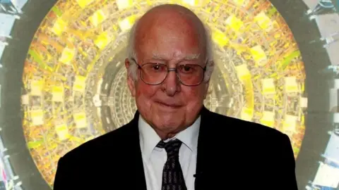 PA Prof Higgs is looking at the camera. He is bald apart from some white tufts of hair at the sides of his head. He is wearing glasses and a dark suit and tie.There is a bright yellow and green circular background 