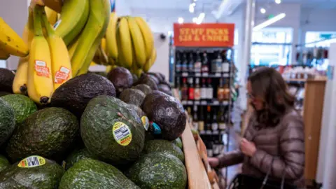 Bloomberg via Getty Images Avocados and bananas at grocery store in San Francisco, California, US, with someone in a puffer coat in the background