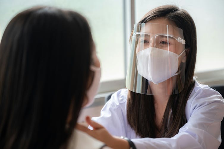 A health-care worker wearing a face mask and a patient with their back to the camera