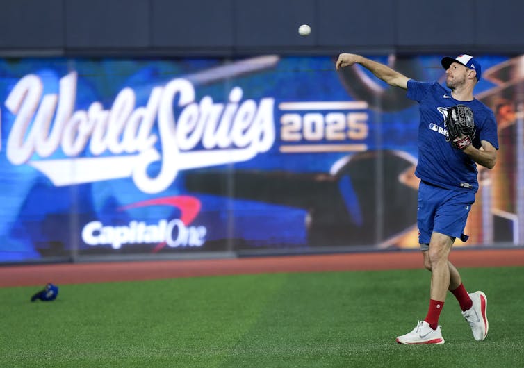 A baseball player throws a ball while standing in front of a sign that says World Series 2025