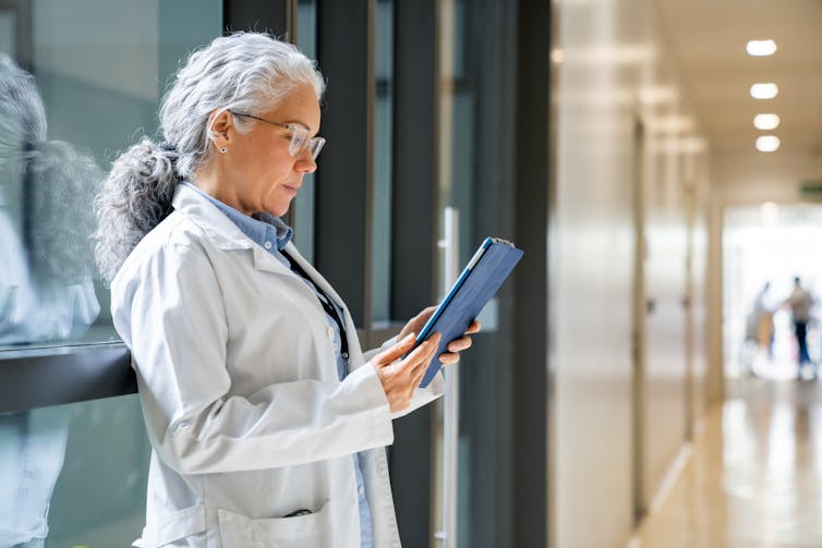 Female doctor reading a medical chart on a digital tablet in a hospital hallway.