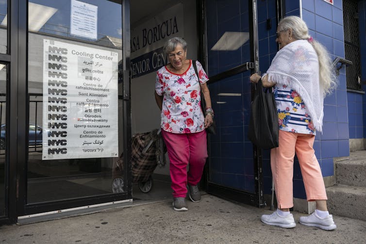 A older man holds a door for a woman at a cooling center.