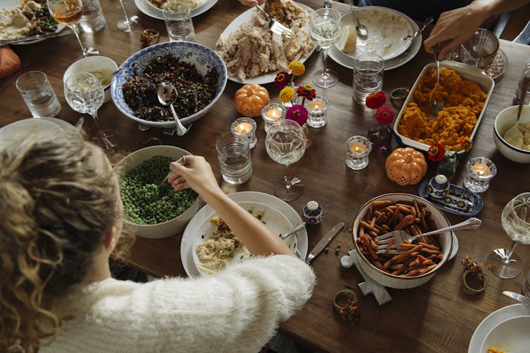 Person scooping a spoonful of peas from a table laden with Thanksgiving food
