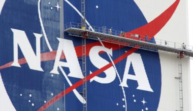 workers on scaffolding paint a nasa logo on a massive white building