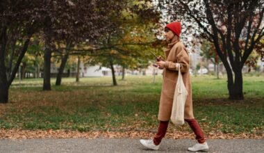 A person with brown hair up in a bun walking a white dog in a park surrounded by trees.