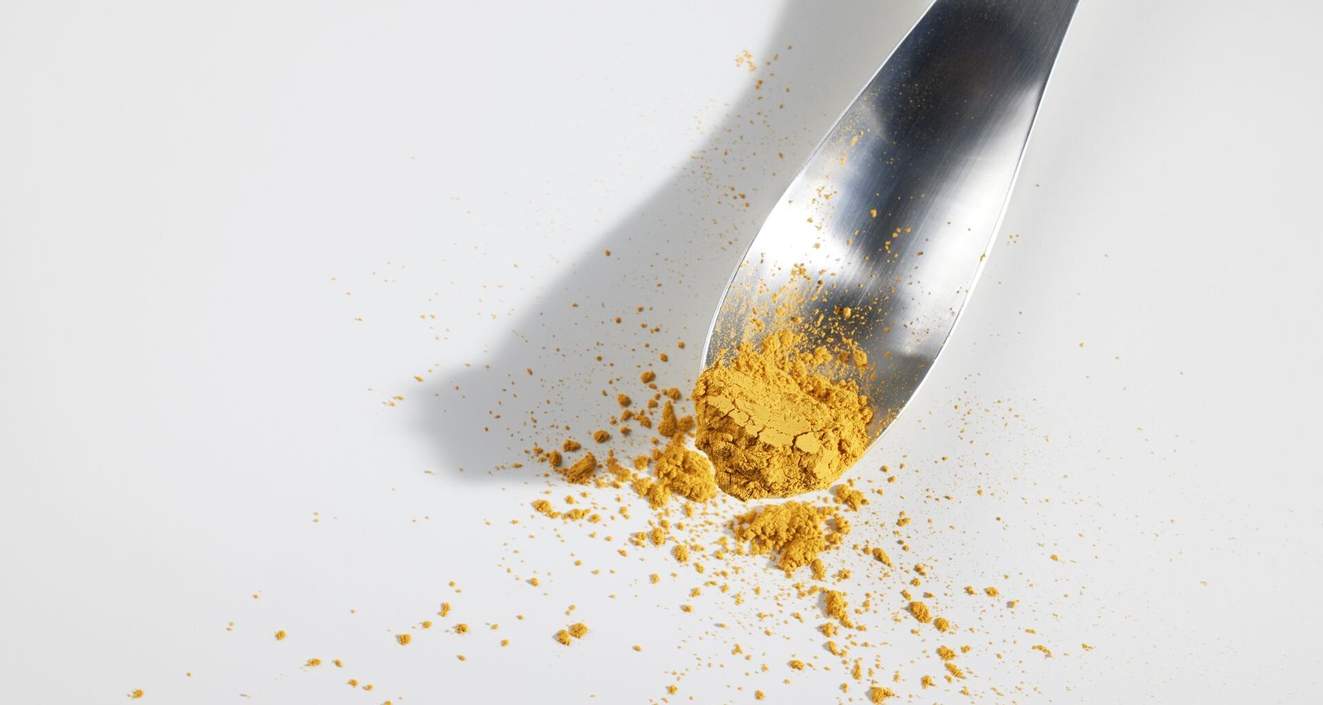 A metal spoon holds a yellow powder over a white surface