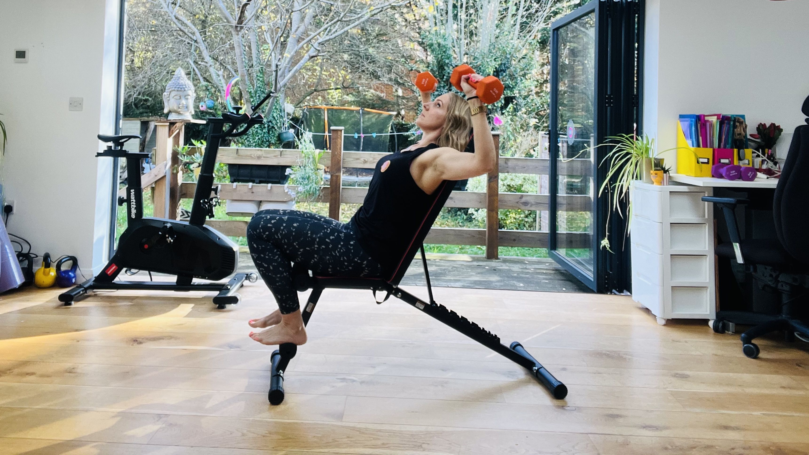Woman exercising at home using dumbbells and a weight bench