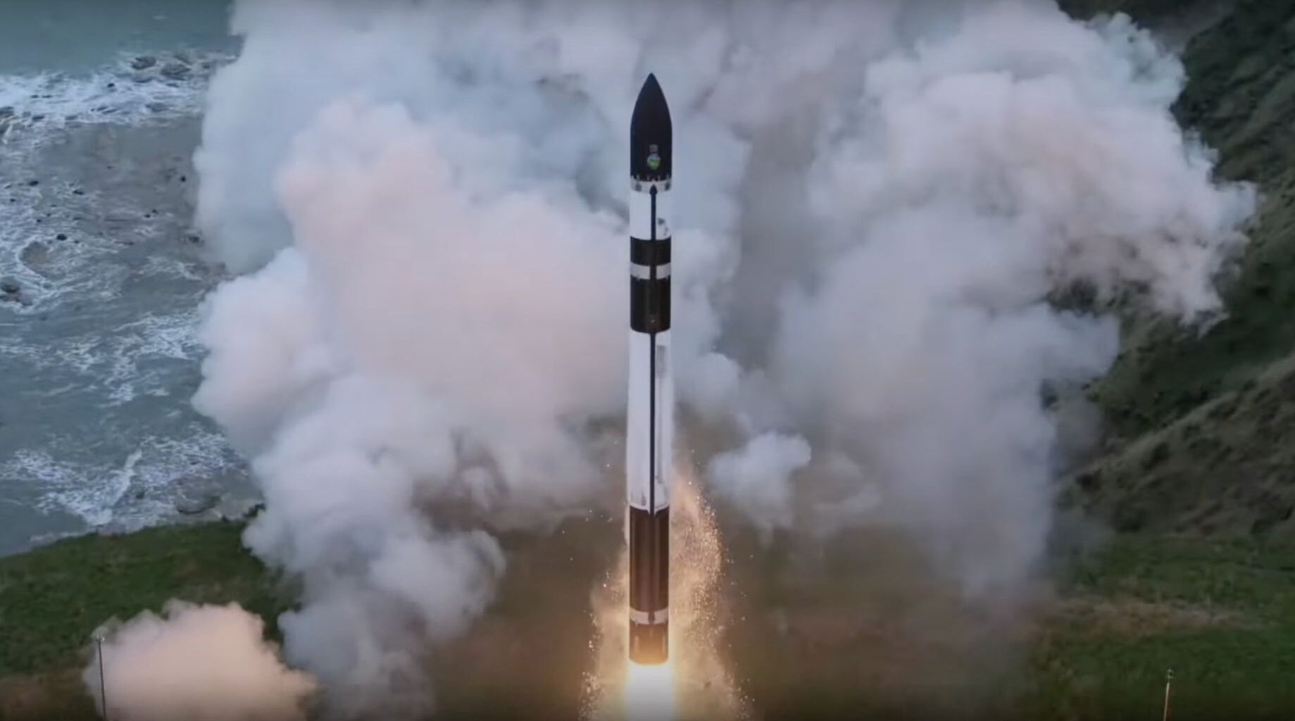 a black and white rocket launches from a seaside pad