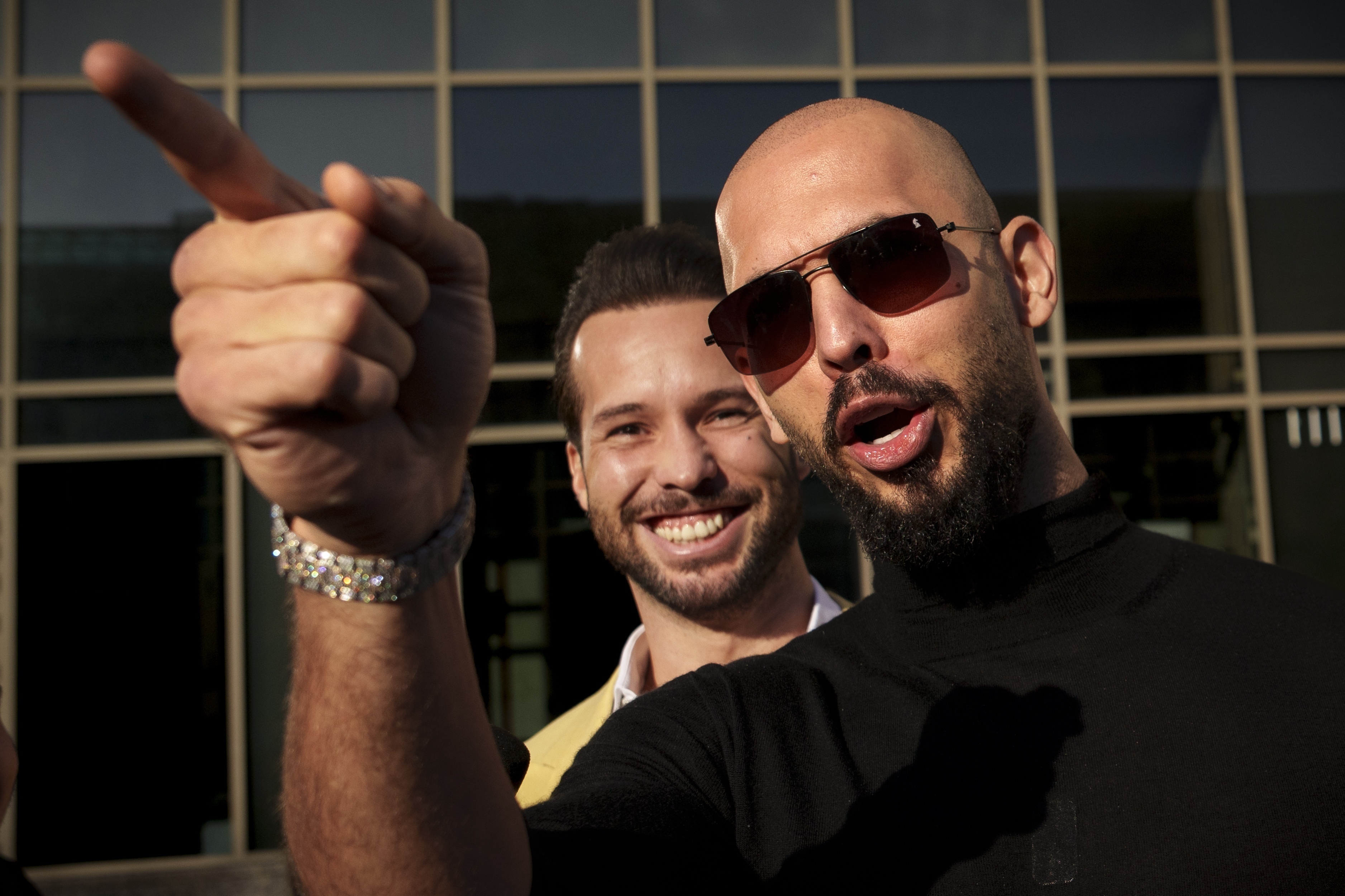Andrew Tate gestures while wearing sunglasses, next to his brother Tristan, outside the Bucharest Tribunal.