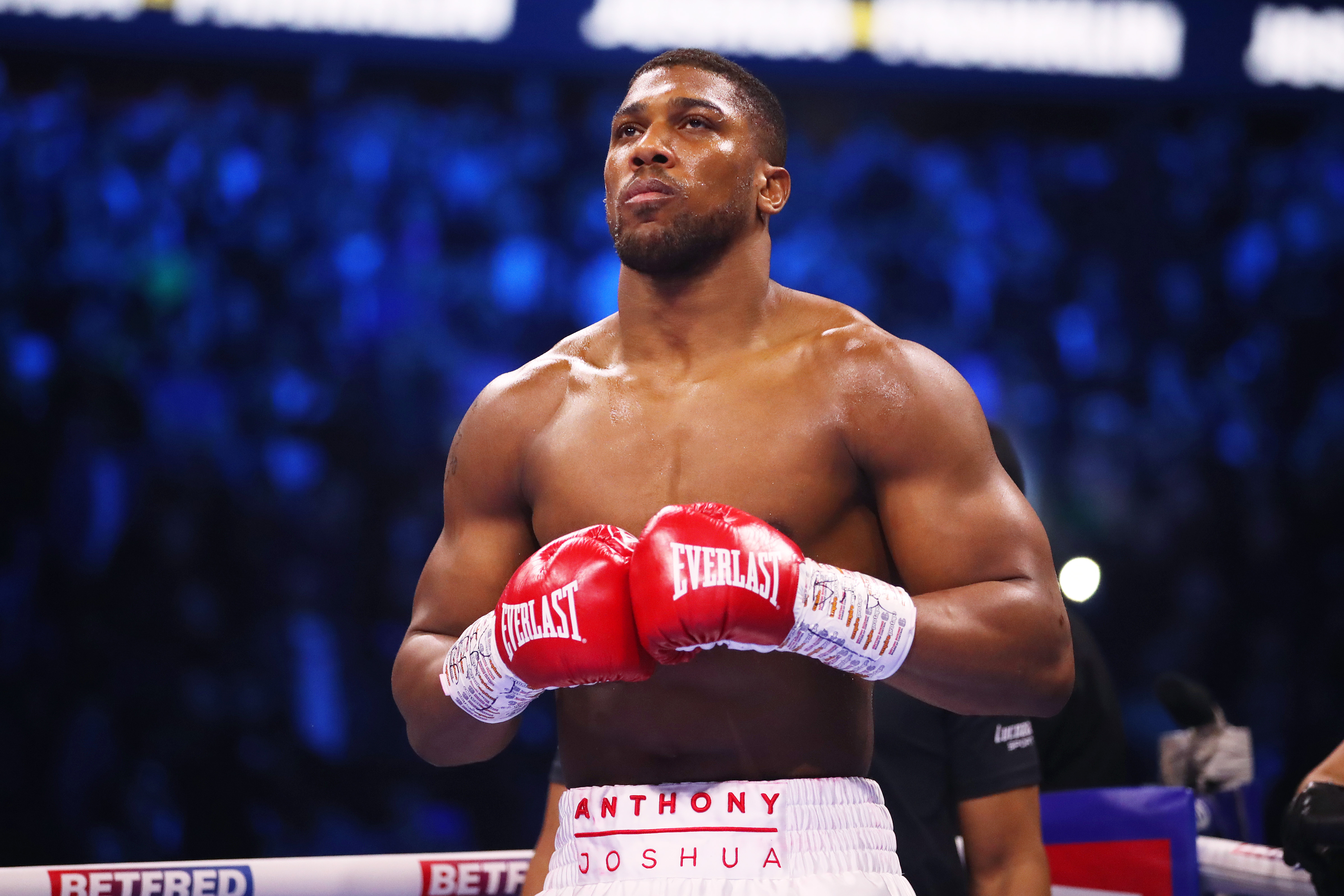Anthony Joshua in red boxing gloves looking toward the ring before a heavyweight fight.