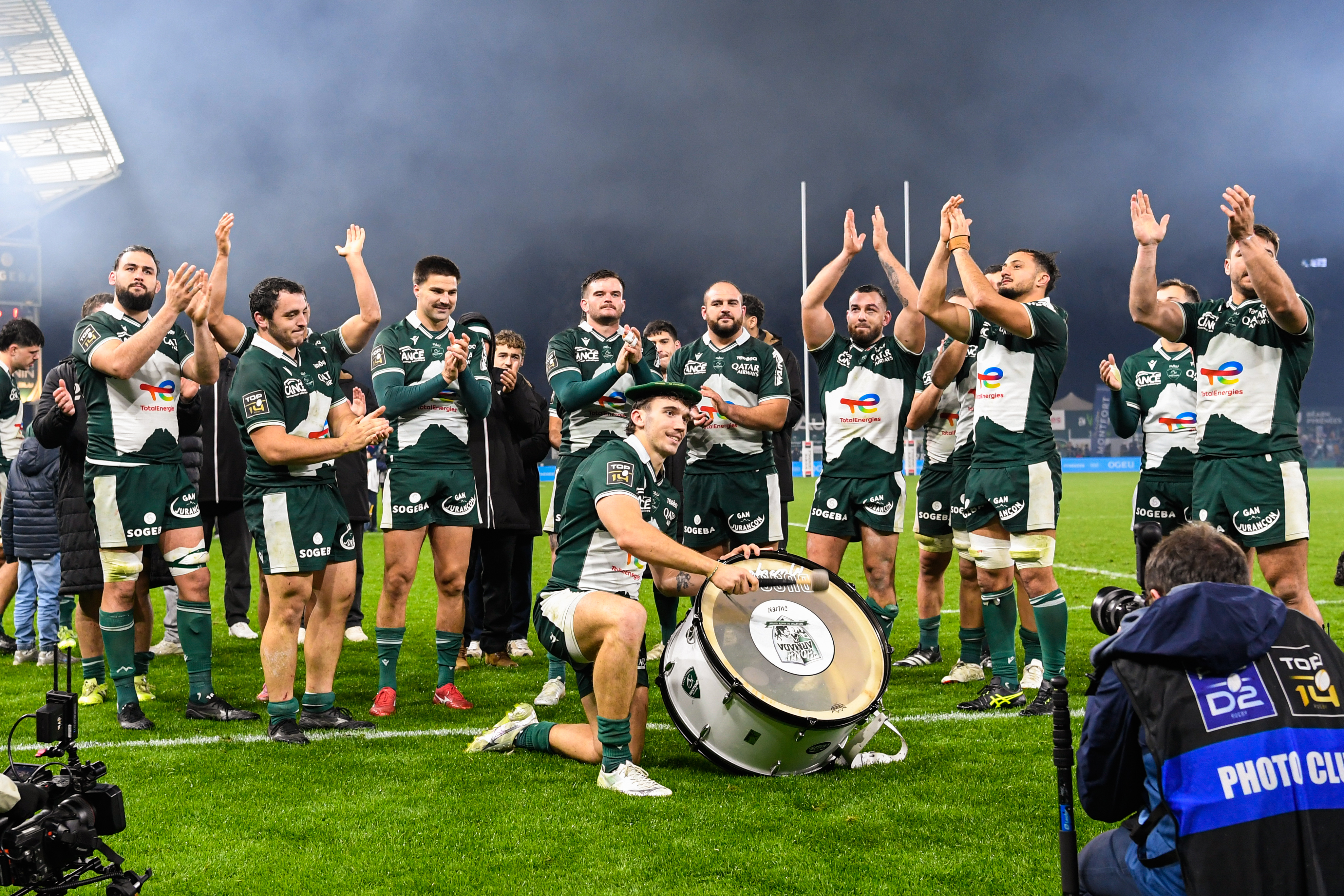 Rugby player Fabien Brau-Boirie of Pau kneeling with a drum, surrounded by celebrating teammates.