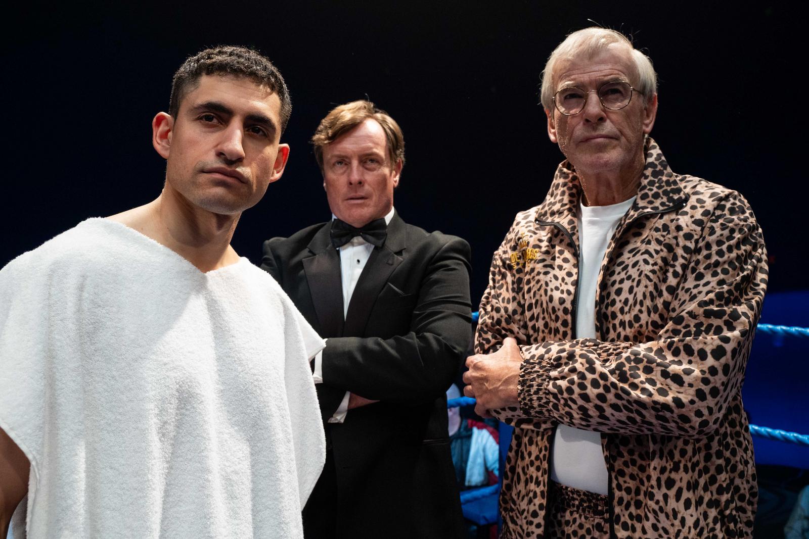 Film still from "Giant (2025)" featuring Amir El-Masry as Naseem Hamed, Toby Stephens as Frank Warren, and Pierce Brosnan as Brendan Ingle.