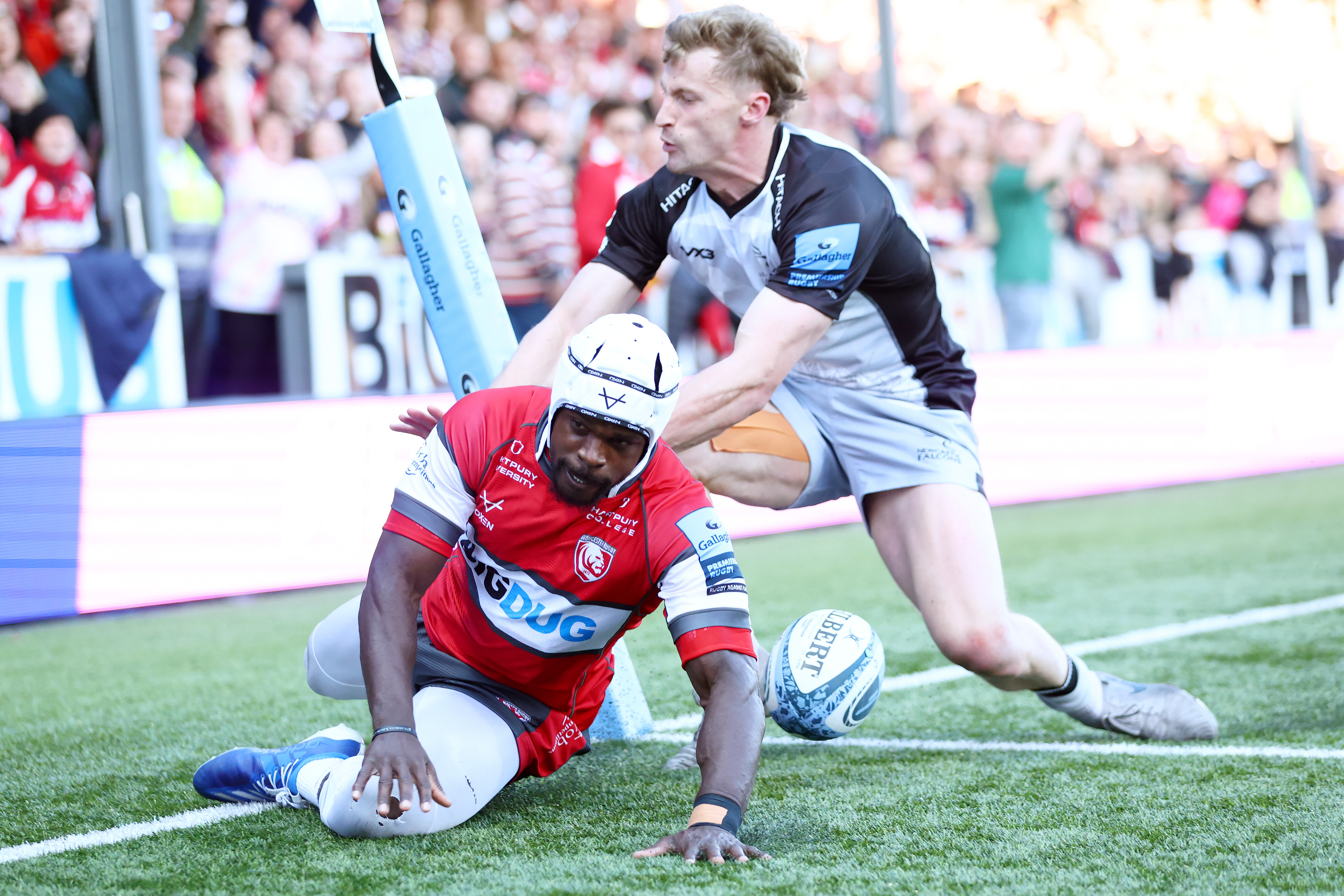 Christian Wade of Gloucester scoring a try while a Newcastle Falcons player attempts to stop him.
