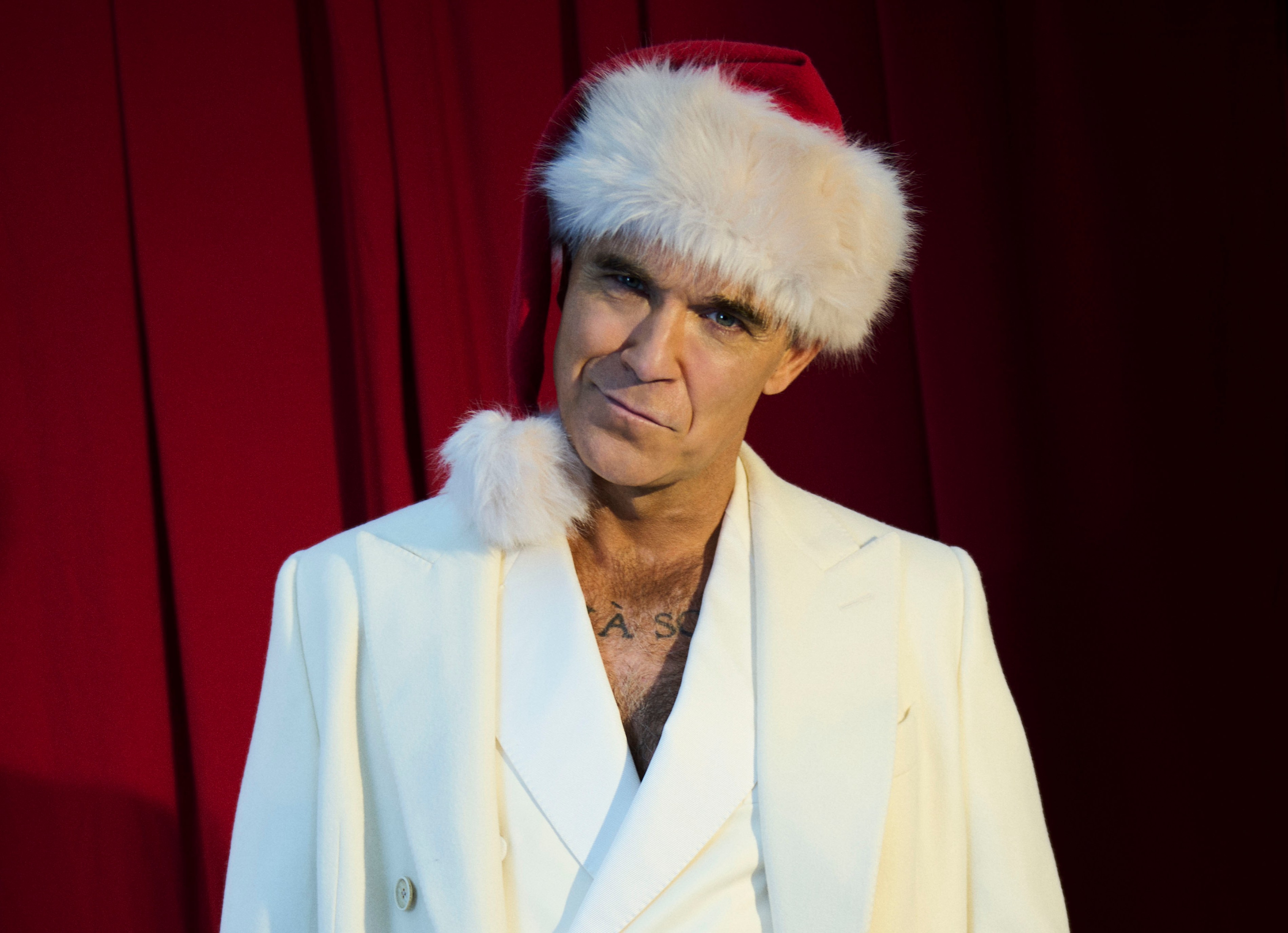 Robbie Williams wearing a white suit and Santa hat.