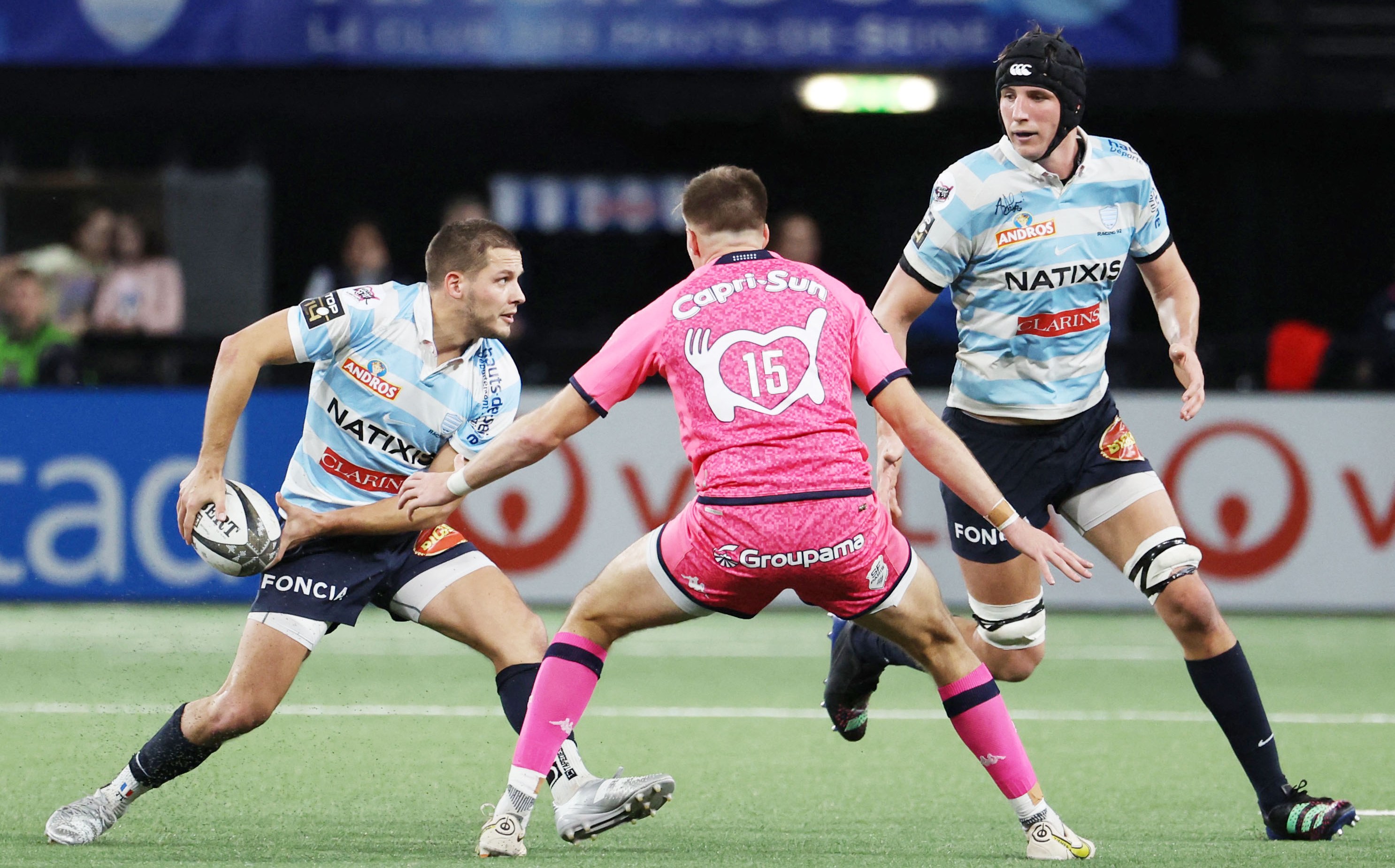 Racing92's Antoine Gibert (left) passes the ball next to Stade Francais' Leo Barre (center) during a rugby match.