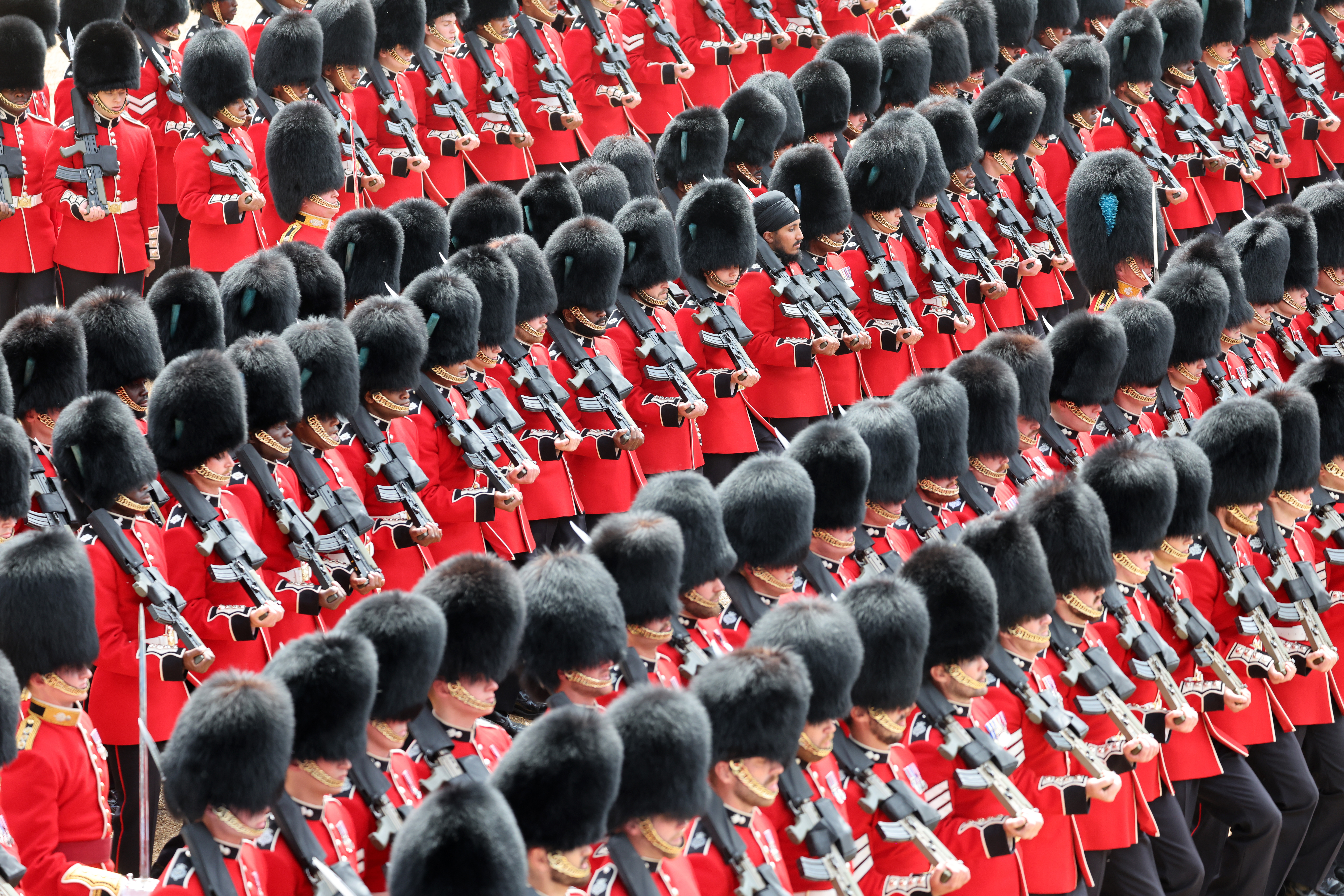 Soldiers of the Guards division in red coats and tall black hats on parade.