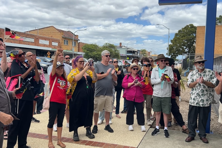 A crowd with some holding Aboriginal flags pay their respects