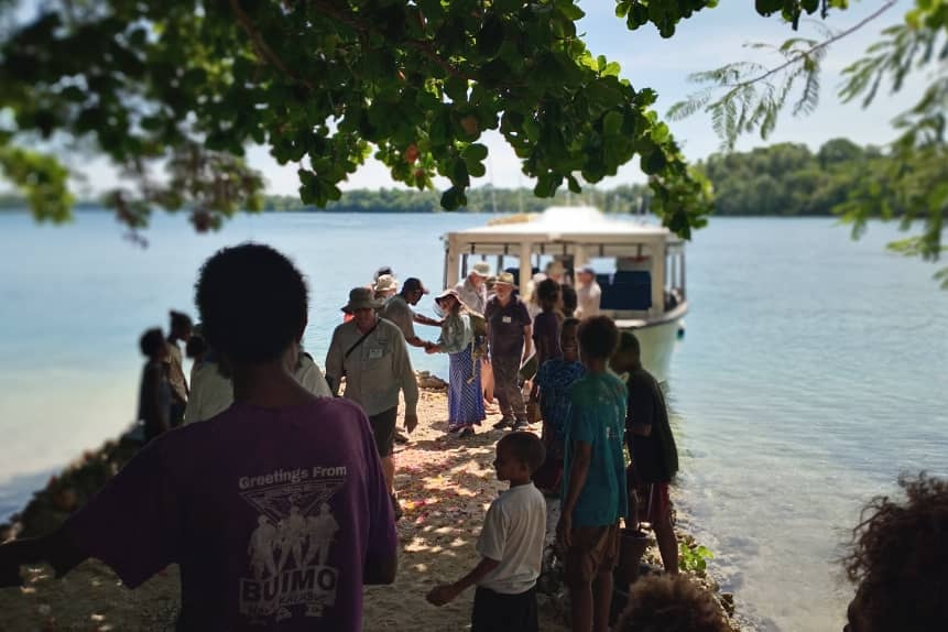 Tourists disembark a small boat and are greeted by village residents in PNG.