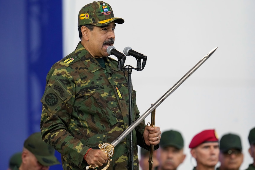 Nicolas Maduro in green camouflage clothing speaking into a microphone and holding a long silver sword