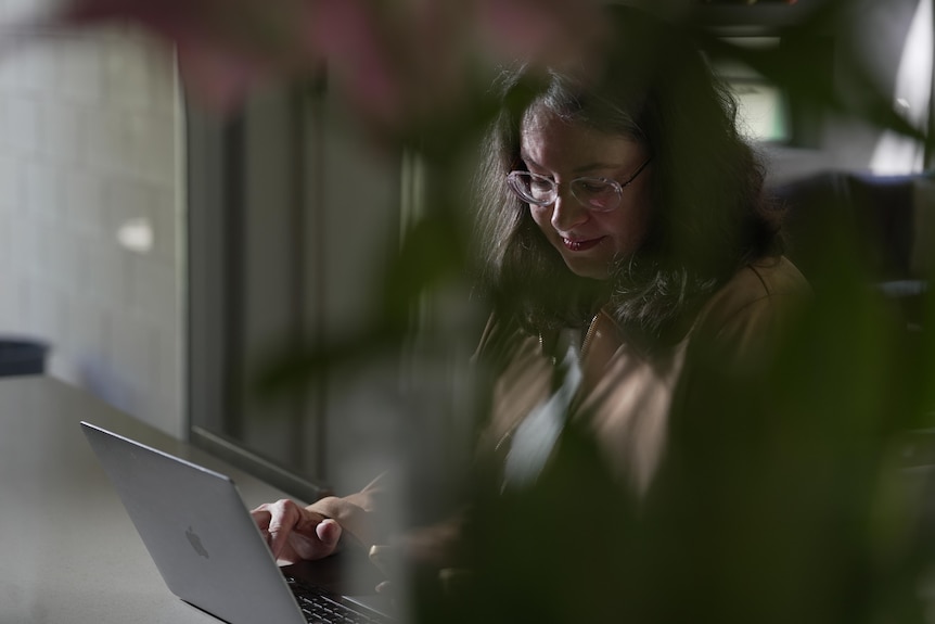 A woman looks at a laptop with a plant in the foreground.