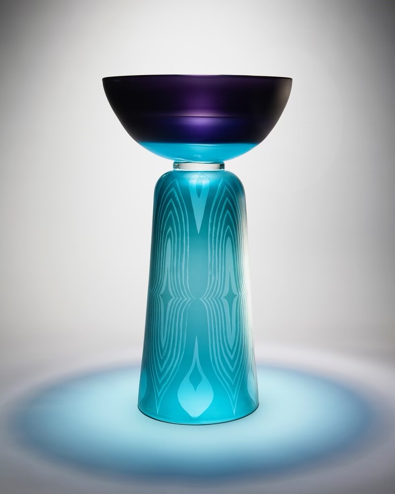 A glass sculture with a tall, light blue patterned base and a purple bowl on top.