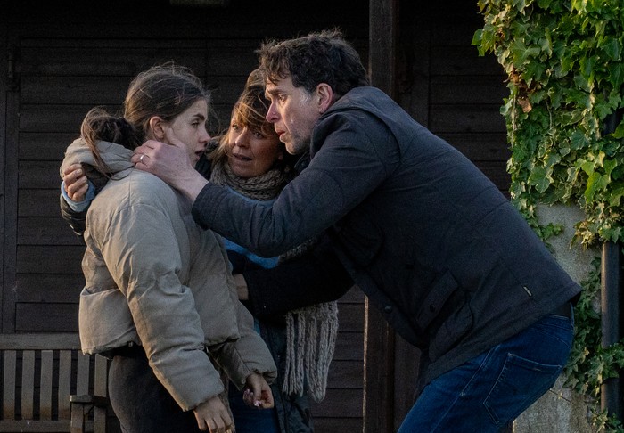 A panicked Marlon grabs April's face as Rhona holds onto her shoulder in a scene from Emmerdale