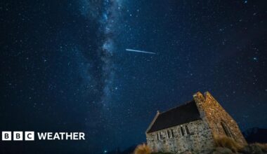 Streak of light in star-filled dark night sky above a church