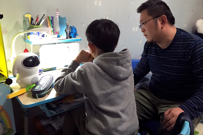 A Chinese child doing homework next to his father.