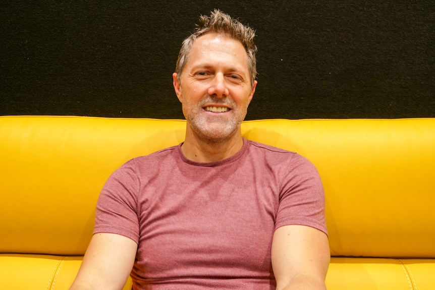A man sits on a yellow couch. 