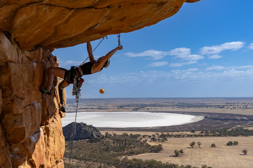 Climber Sarah Larcombe approaches a horizontal roof while on Mount Arapiles. The Australian outback is in the background.