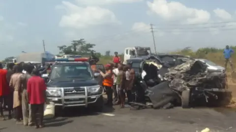 Federal Road Safety Corps An image of a police car parked next to the wreckage, with a crowd gathered around it