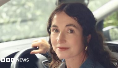 Kyle Sieniawski, laughing. Kyle has a huge smile, large black-rimmed glasses and wears a grey hooded top.