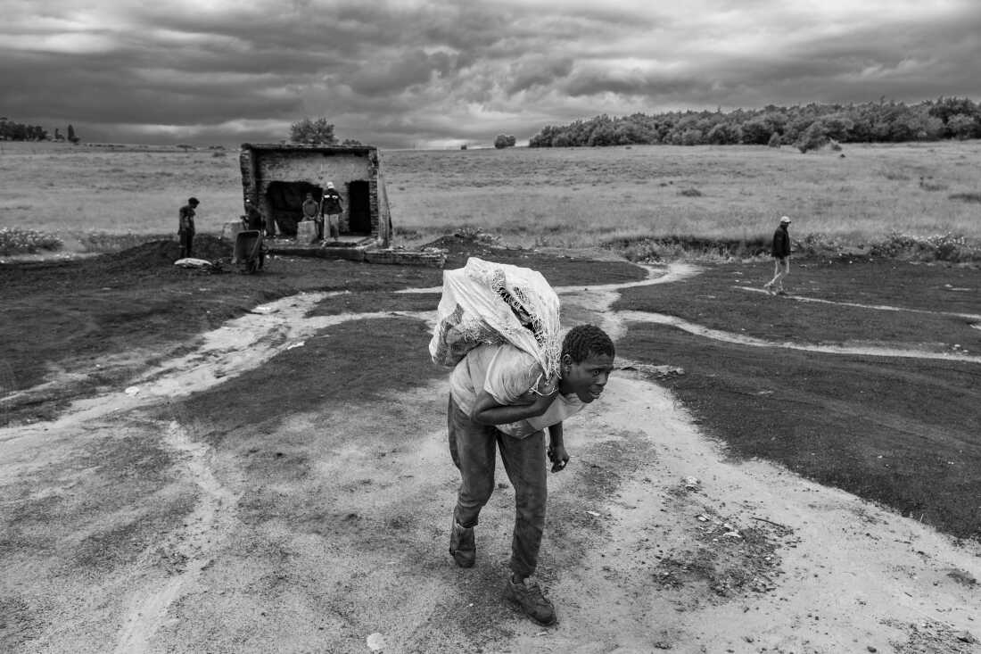 Artisanal coal miner Emmanuel Siyabonga hauls a sack of coal to a client's car at the abandoned Golfview coal mine in Ermelo, South Africa. The work is grueling and hazardous but is one of the few viable means of making a living in a town with widespread poverty and high rates of unemployment.