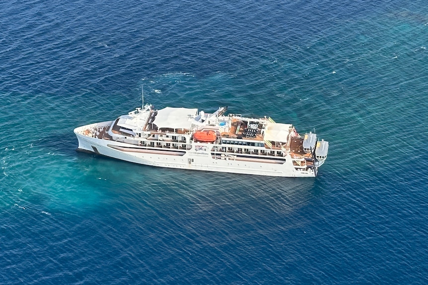 An aerial view of a white cruise ship stranded on a patch of reef surrounded by deeper water.