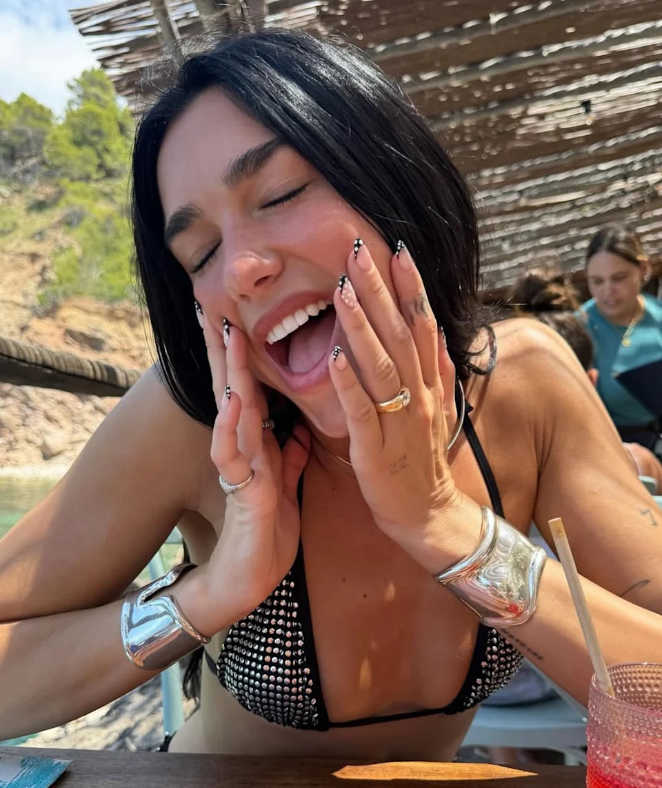person seated at a table with a drink outdoors under natural light
