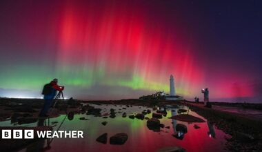 A close-up image of the Sun’s surface, showing a bright orange colour with white sunspots and an active solar flare region featuring a white burst.
