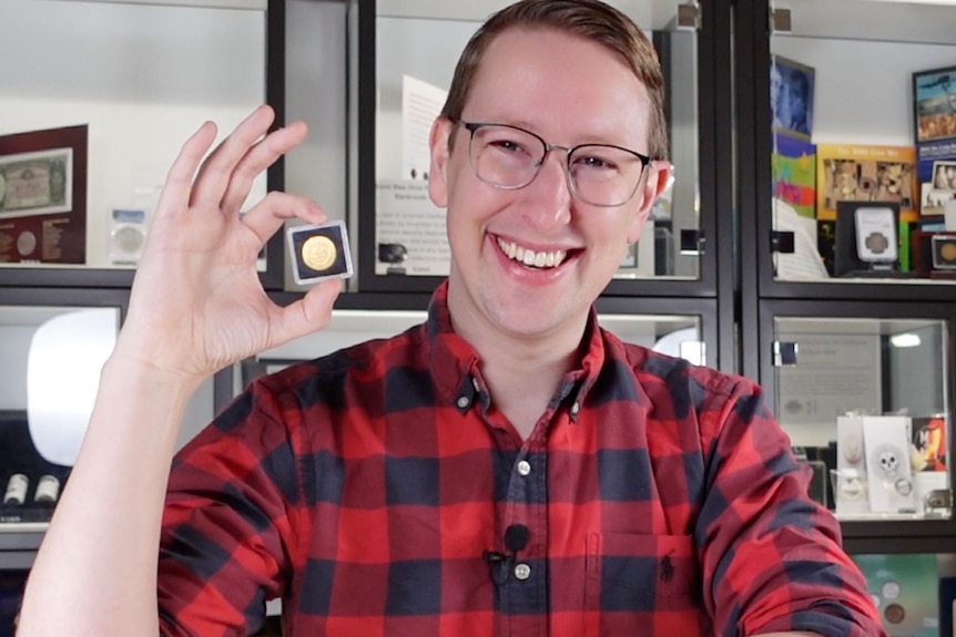 A man in glasses and a red-checked shirt holding an old coin in a case.