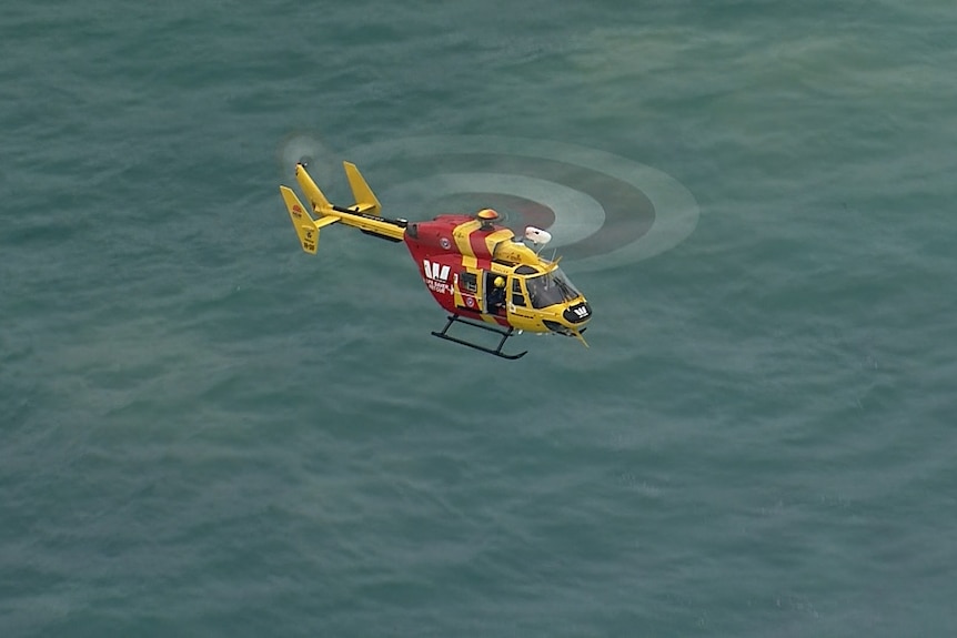 An aerial of the helicopter, yellow and red, over ocean.