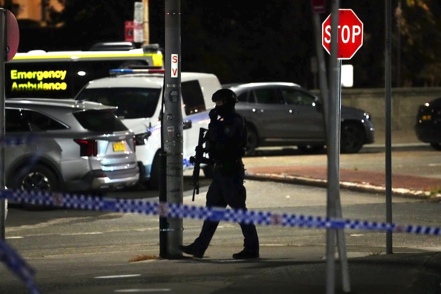 An armed police officer in a cordoned off street at night.