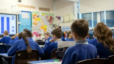 PA Media A group of year five pupils sat down facing the front of a classroom. The students are wearing blue jumpers and blue polo shirts and none of their faces are visible.