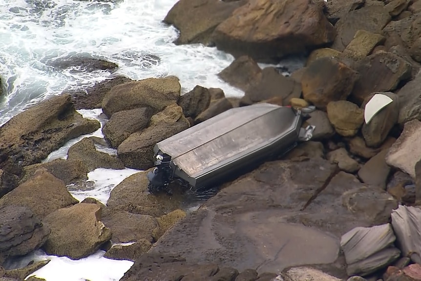 A boat dingy capsized on rocks near ocean.