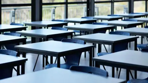 Getty Images A set of empty chairs, sat at standalone desks in a brightly-lit room.