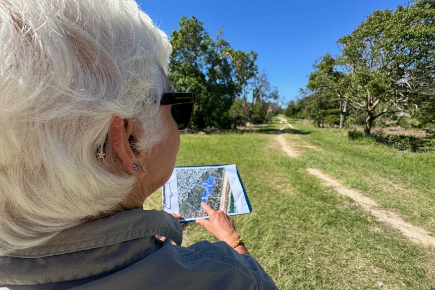 A woman stands with a map and points out where trees will be planted