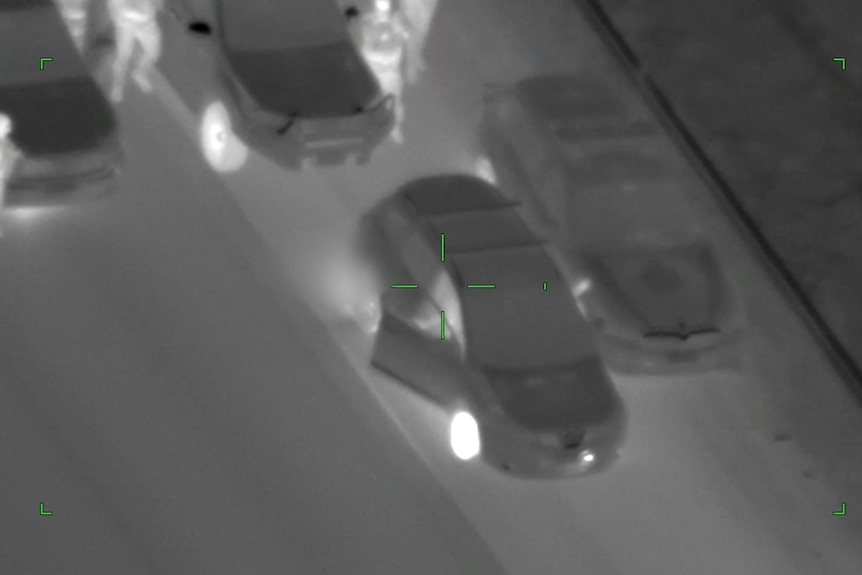 Black and white grainy footage shows a car stopped on a road with police approaching.